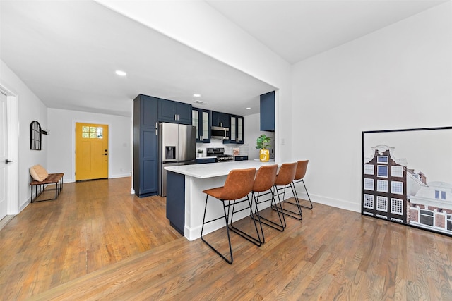 kitchen featuring glass insert cabinets, a peninsula, appliances with stainless steel finishes, wood finished floors, and a breakfast bar area