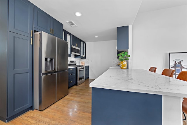 kitchen featuring visible vents, appliances with stainless steel finishes, a breakfast bar, a peninsula, and blue cabinetry