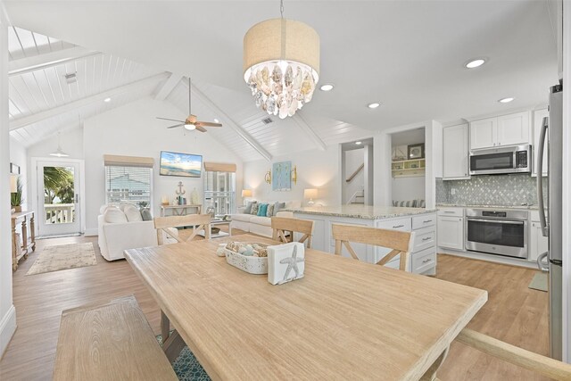 dining area with stairs, light wood-style flooring, ceiling fan with notable chandelier, and beam ceiling