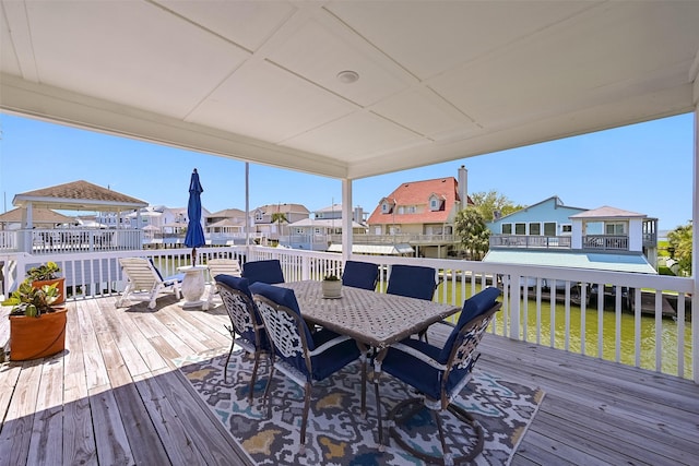 wooden terrace with outdoor dining area, a lawn, a residential view, and a water view
