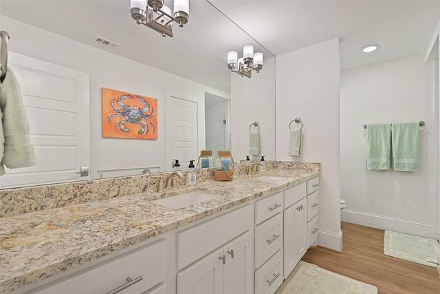 bathroom featuring visible vents, toilet, wood finished floors, a sink, and double vanity