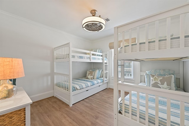 bedroom featuring visible vents, baseboards, crown molding, and wood finished floors