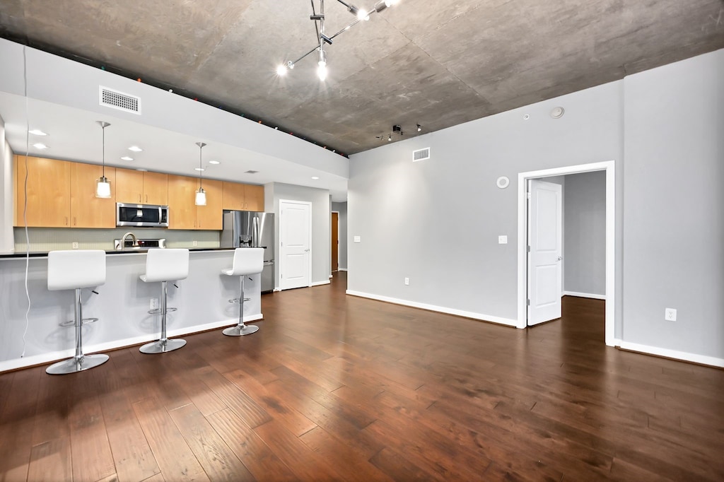 kitchen featuring dark wood finished floors, visible vents, a breakfast bar, stainless steel appliances, and decorative light fixtures