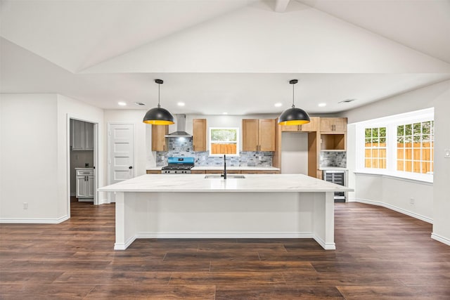 kitchen with a sink, a center island with sink, gas range, decorative backsplash, and wall chimney range hood
