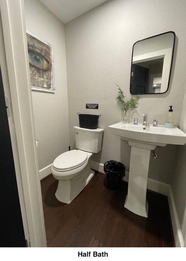 half bathroom featuring wood finished floors, toilet, and baseboards