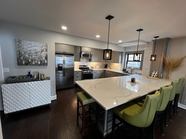 kitchen with stainless steel appliances, a peninsula, dark wood finished floors, gray cabinetry, and light stone counters