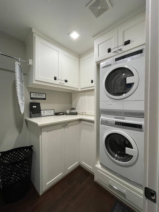 laundry area with cabinet space, stacked washer / drying machine, dark wood-type flooring, and visible vents
