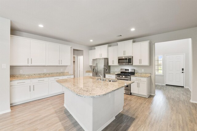 kitchen featuring stainless steel appliances, a sink, light wood finished floors, a center island with sink, and white cabinetry
