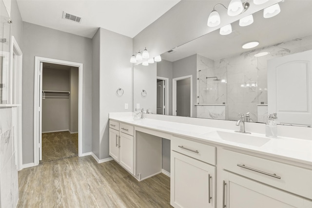 full bathroom with a marble finish shower, double vanity, wood finished floors, a spacious closet, and baseboards