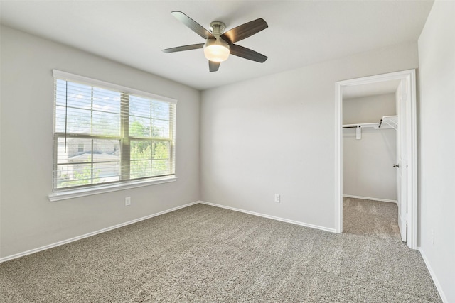 unfurnished bedroom featuring carpet floors, a walk in closet, baseboards, a closet, and ceiling fan