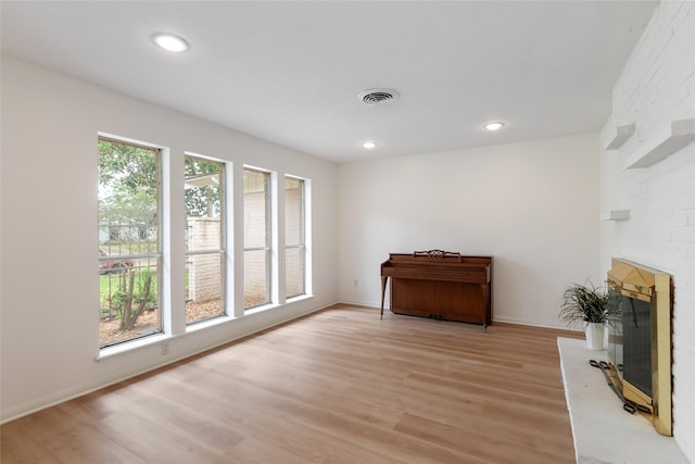 living room with light wood-style flooring, visible vents, recessed lighting, and a brick fireplace