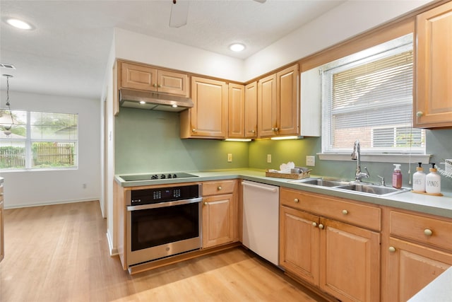 kitchen featuring stainless steel oven, under cabinet range hood, a sink, and light wood-style flooring