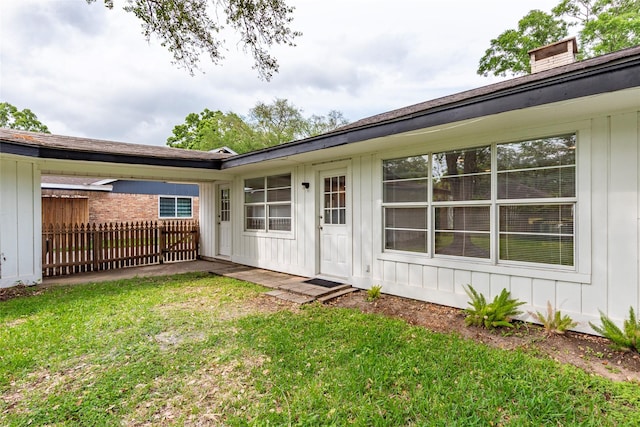 entrance to property featuring board and batten siding, a yard, and fence