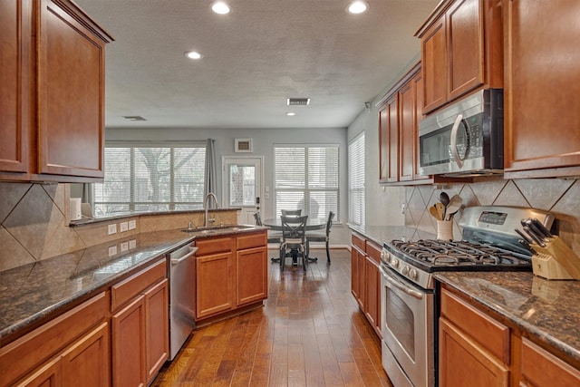 kitchen with stainless steel appliances, a sink, recessed lighting, dark wood finished floors, and brown cabinetry