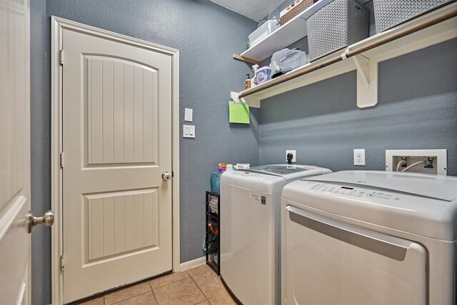 washroom featuring independent washer and dryer, light tile patterned floors, baseboards, and a textured wall