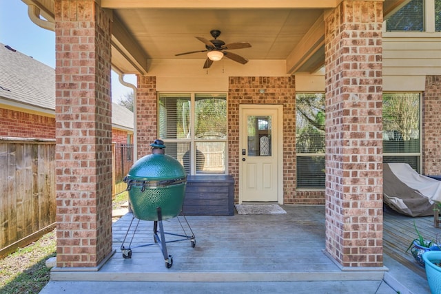 entrance to property with a ceiling fan, fence, brick siding, and a deck