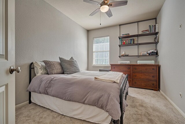 bedroom featuring light colored carpet, baseboards, a textured wall, and ceiling fan