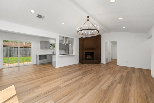 1802 Winston Homestead St, Richmond, TX 77406 - unfurnished living room with visible vents, an inviting chandelier, a brick fireplace, lofted ceiling with beams, and light wood-type flooring