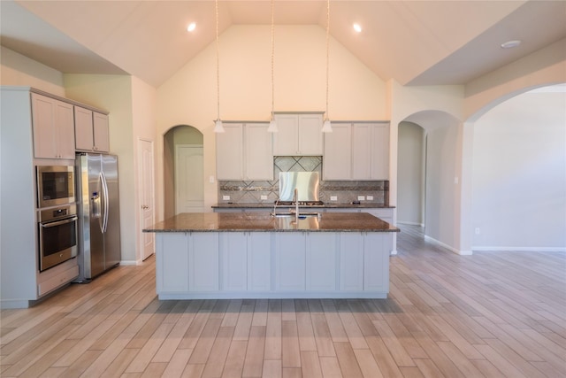 kitchen featuring a sink, high vaulted ceiling, arched walkways, and stainless steel appliances
