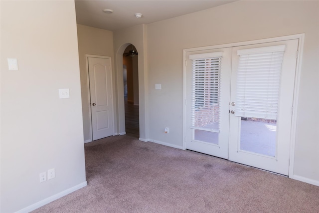 empty room featuring arched walkways, french doors, baseboards, and carpet