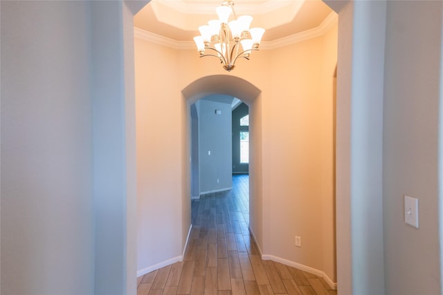 hallway with a raised ceiling, arched walkways, a notable chandelier, crown molding, and light wood finished floors