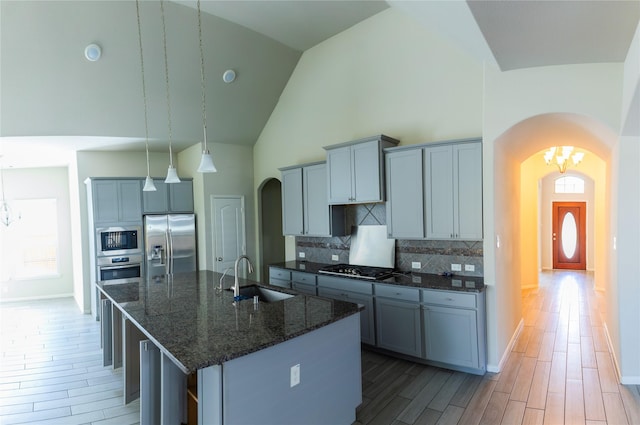 kitchen featuring a sink, high vaulted ceiling, arched walkways, and stainless steel appliances
