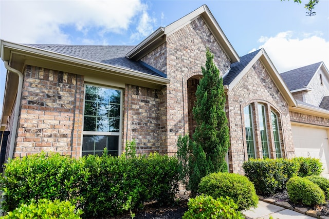 view of front of home featuring brick siding, an attached garage, a shingled roof, and stone siding