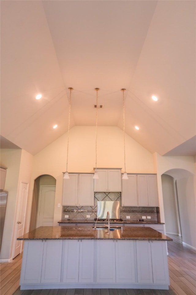 kitchen featuring arched walkways, high vaulted ceiling, decorative backsplash, and a sink
