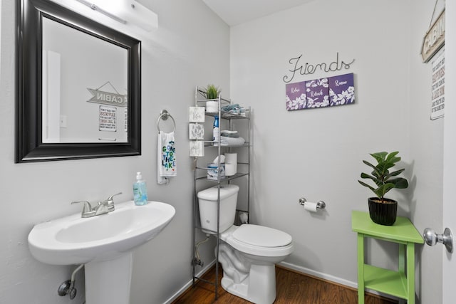 half bathroom with toilet, baseboards, a sink, and wood finished floors