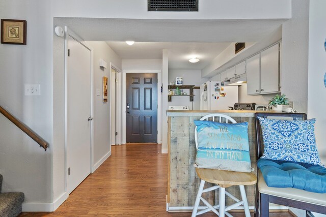 kitchen with white cabinets, freestanding refrigerator, baseboards, wood finished floors, and visible vents