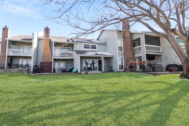 back of property with a lawn, a balcony, and a chimney