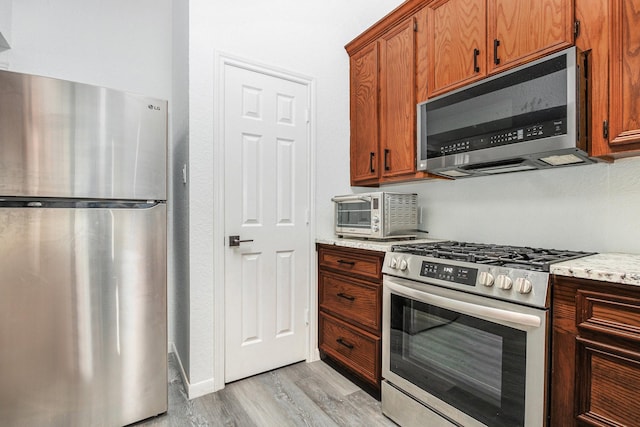 39 Alexander Ct, Angleton, TX 77515 - kitchen with appliances with stainless steel finishes, light wood-style floors, brown cabinets, and light stone countertops