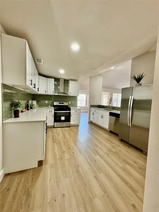 kitchen featuring wall chimney range hood, stainless steel appliances, visible vents, and light wood-type flooring