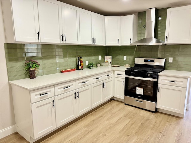 kitchen with white cabinets, wall chimney exhaust hood, stainless steel gas range oven, and light wood-type flooring
