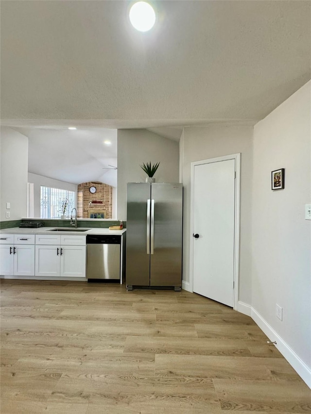 kitchen with a sink, light wood-style floors, stainless steel appliances, white cabinets, and lofted ceiling