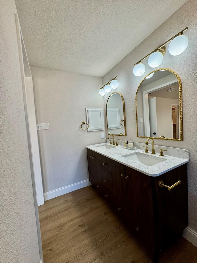 full bath featuring double vanity, wood finished floors, a textured ceiling, and a sink