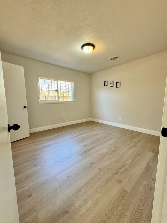 unfurnished room with visible vents, baseboards, wood finished floors, and a textured ceiling