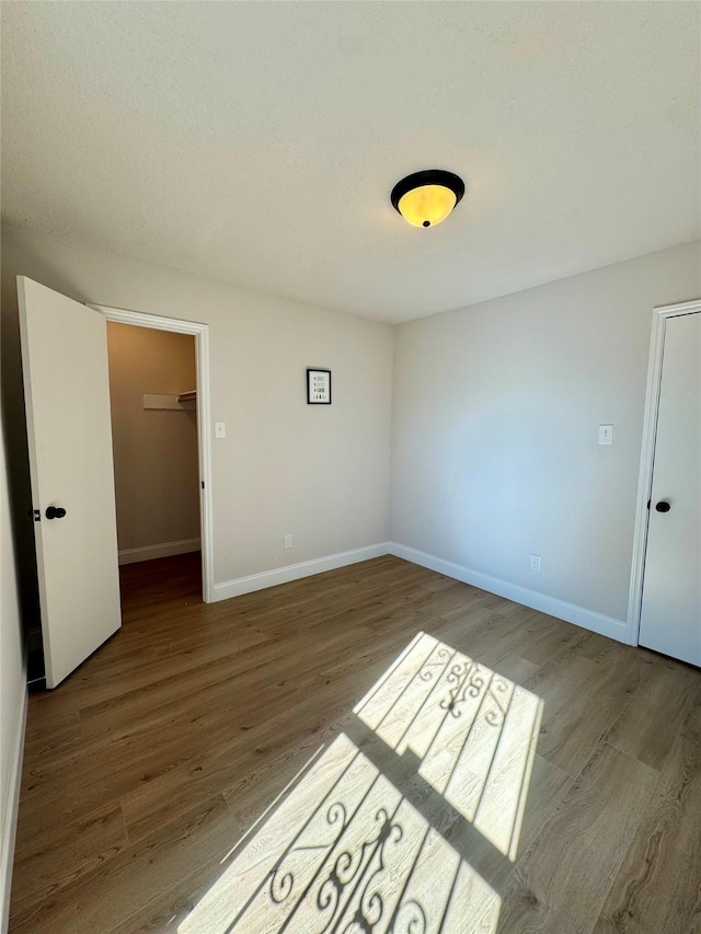 unfurnished bedroom with a spacious closet, wood finished floors, a closet, and baseboards