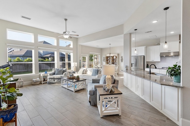 living area featuring visible vents, light wood-type flooring, recessed lighting, and ceiling fan with notable chandelier
