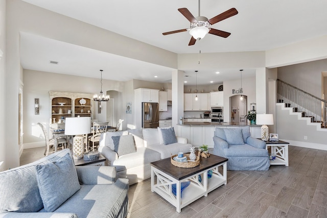 living area featuring light wood-style floors, stairs, visible vents, baseboards, and ceiling fan with notable chandelier