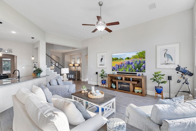 living room featuring stairway, ceiling fan, visible vents, baseboards, and light wood-type flooring