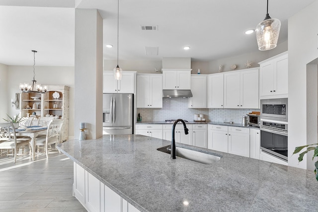 kitchen with stainless steel appliances, under cabinet range hood, decorative backsplash, and a sink