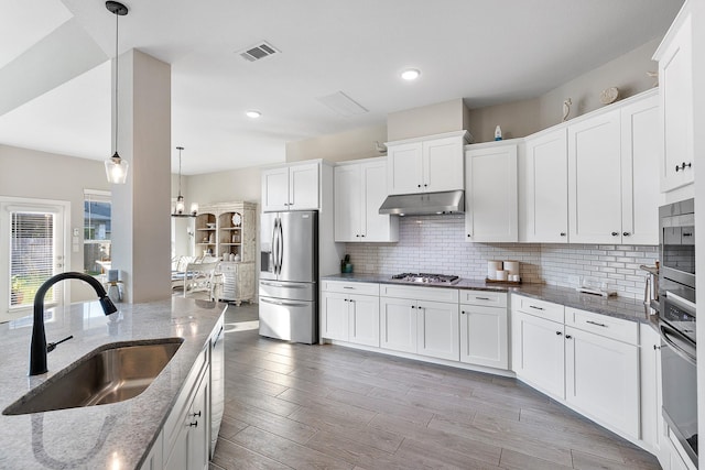 kitchen featuring tasteful backsplash, stainless steel appliances, under cabinet range hood, a sink, and visible vents