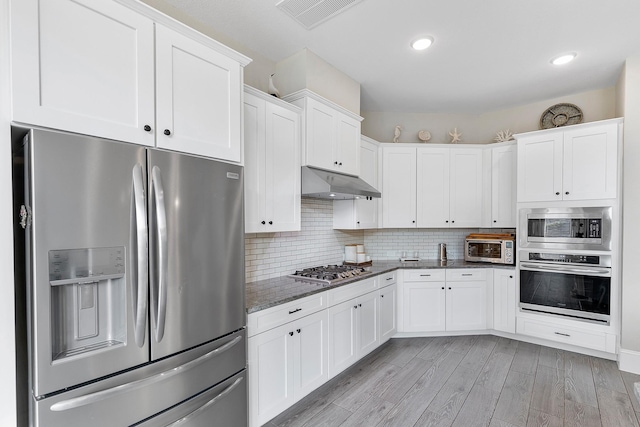 kitchen with dark stone counters, under cabinet range hood, appliances with stainless steel finishes, white cabinets, and visible vents