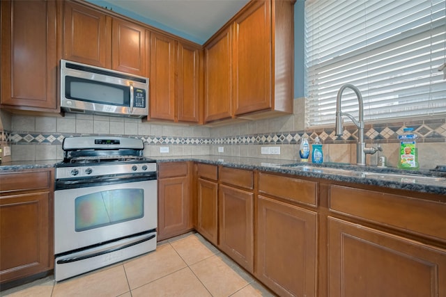 kitchen with a sink, dark stone counters, brown cabinetry, and stainless steel appliances
