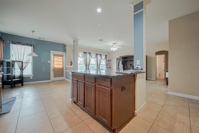 kitchen with baseboards, ornate columns, dark stone counters, a ceiling fan, and light tile patterned floors