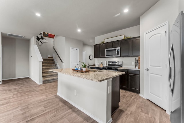 kitchen featuring light stone counters, recessed lighting, a center island with sink, light wood-style floors, and stainless steel appliances