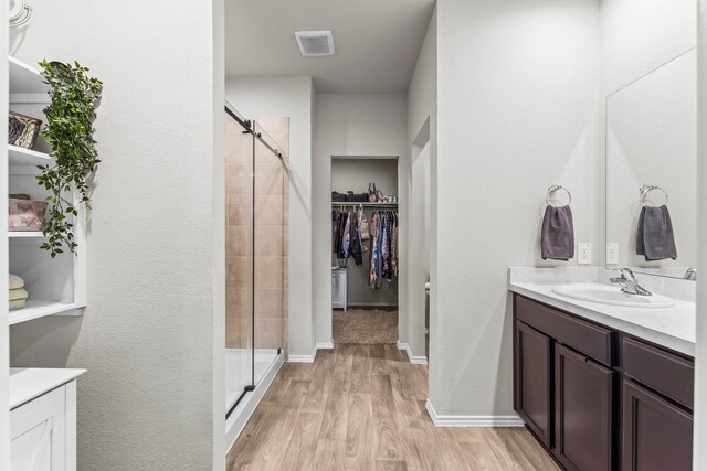 full bathroom with a stall shower, wood finished floors, vanity, and a walk in closet