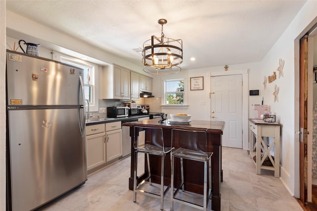2216 Grover Ave, Galveston, TX 77551 - kitchen featuring appliances with stainless steel finishes, a chandelier, a kitchen island, under cabinet range hood, and backsplash