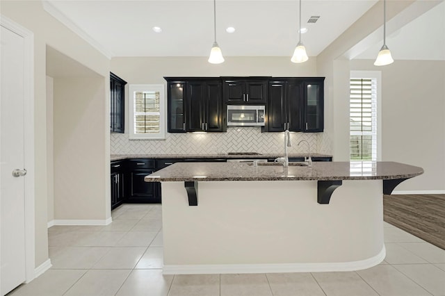 kitchen featuring dark stone counters, tasteful backsplash, a breakfast bar area, stainless steel microwave, and dark cabinets